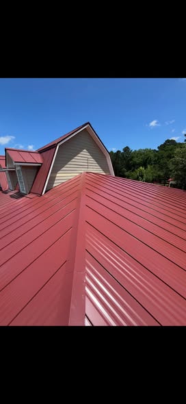 Close view of a red standing seam metal roof meeting a dormer and light siding under a clear sky