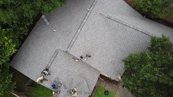 Overhead drone view of a crew working on a grey shingle roof with a ladder at the eaves